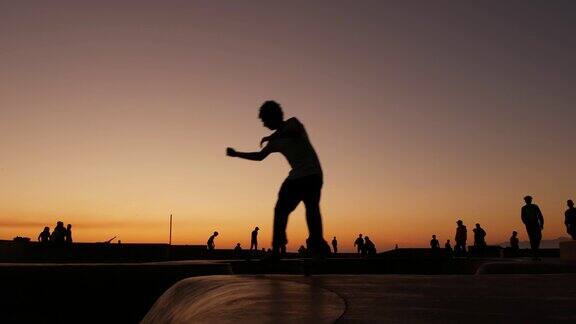 剪影的年轻跳高滑板骑长板夏季日落的背景威尼斯海洋海滩滑板公园加州洛杉矶青少年在滑板坡道极限公园组的青少年