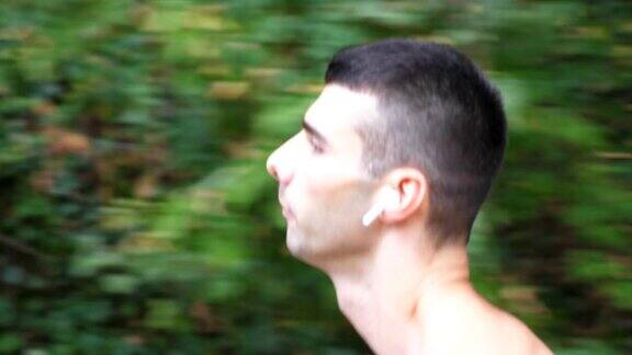 近距离观看年轻强壮的运动员沿着森林附近的小径奔跑运动员戴着无线耳机在初秋慢跑帅哥在户外跑步健康积极的生活方式慢动作