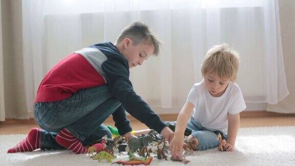 一个金发男孩一个蹒跚学步的男孩和他的哥哥一个十几岁的男孩在家里玩塑料动物玩具