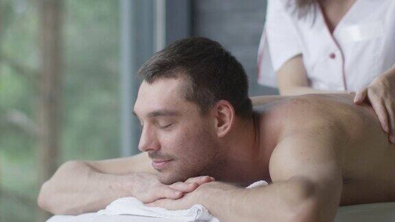 英俊的男人正在享受一个放松按摩从一个女按摩师在健康中心