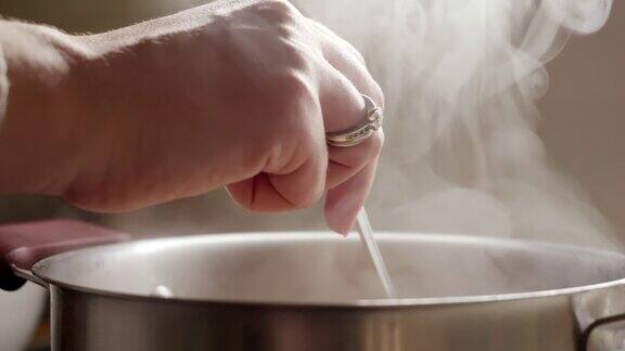 女人煮汤和用勺子搅拌的特写健康营养在家做饭热蒸