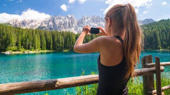 女性游客探索山坡站在湖边被山包围欣赏风景和用智能手机拍照