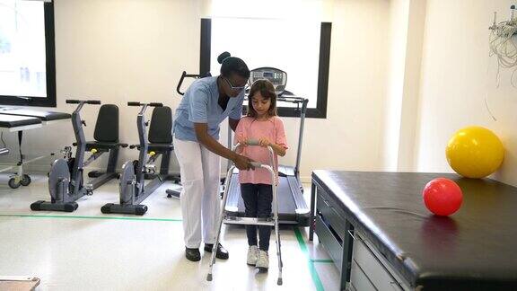 在理疗师的帮助下使用移动助行器的可爱小女孩