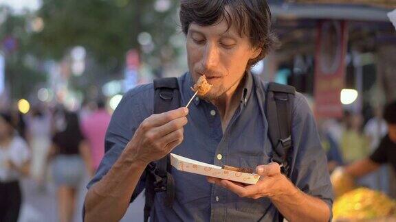 一名年轻人参观传统的韩国街头市场他正用竹竿吃鱼糕去韩国旅游