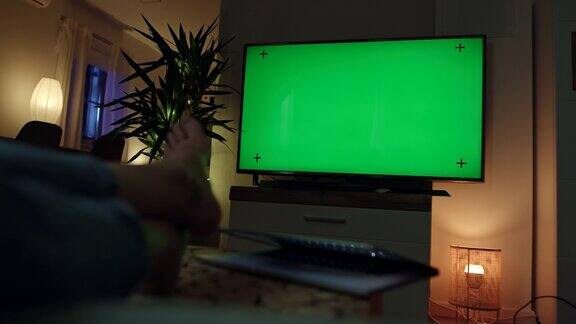 一个无法辨认的女人在看彩色键绿色屏幕的电视