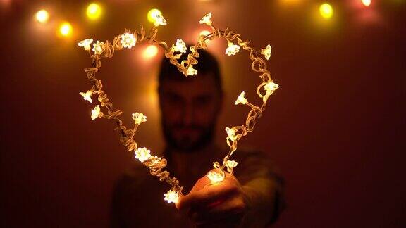 一个男人手里拿着一颗由灯泡做成的心透过它往外看情人节
