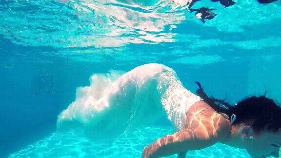 一名身穿白色婚纱扎着辫子的年轻女孩在水下慢动作游泳