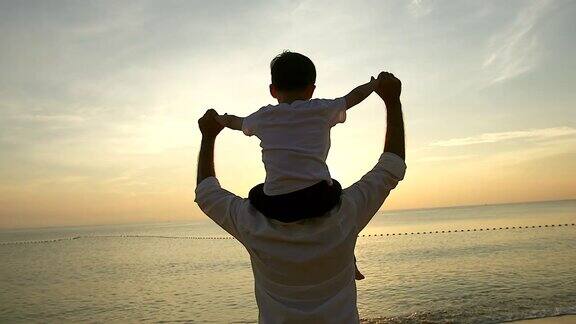 日出时父亲和儿子站在海滩上他们一起度过了宝贵的家庭时光用慢镜头拍摄