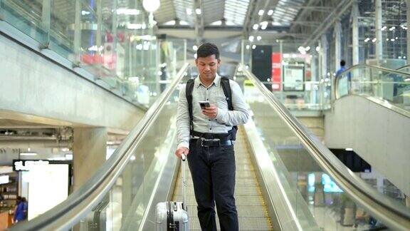 一名年轻人拿着行李箱站在人行道上一边使用智能手机