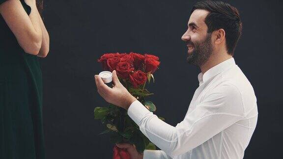 英俊的男人单膝跪地手里拿着戒指和玫瑰向他的女人求婚她说是的