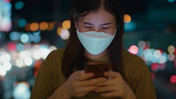 晚上在城市街道上戴着口罩使用手机