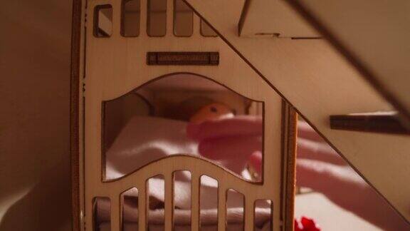 在木制的玩具屋里一个小孩手抓娃娃躺在床上