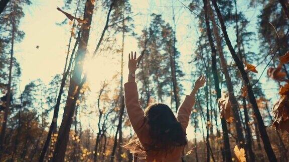 一个快乐的年轻女子在秋天的树林里抛起树叶快乐地旋转着