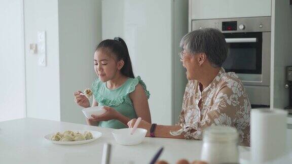 亚裔华人老太太和她的孙女在厨房的柜台上吃饺子