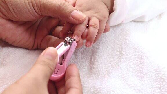妈妈手拿指甲刀在可爱的宝宝睡觉时用小手指剪指甲用爱和关怀保持清洁为人父母和母性健康幸福的家庭