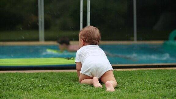 婴儿在后院的草地上爬行观察孩子们在游泳池里玩耍婴儿爬行外