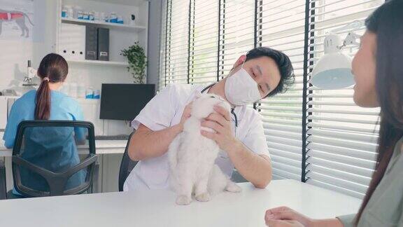 亚洲兽医在兽医诊所预约时为猫检查在宠物医院专业兽医男和小猫主人坐在带着听诊器工作的桌子上检查小动物