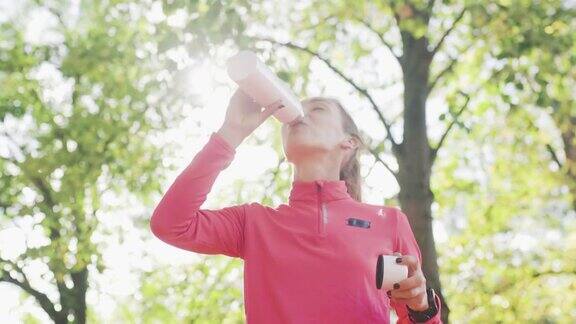 穿着粉色运动服的健身女孩在公园里喝水