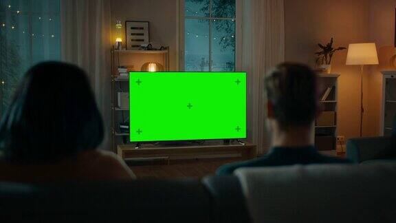 一对夫妇坐在客厅的沙发上看绿色模拟屏幕电视男女朋友的浪漫之夜