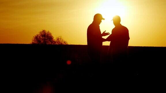 两个农民在田地里坚定地握手他们用平板电脑交流在日落时