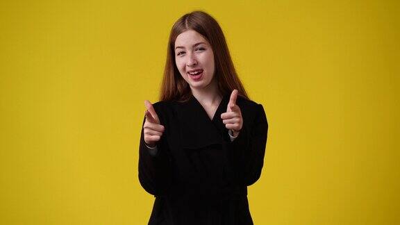 4k视频可爱的女孩指着相机在黄色背景上竖起大拇指