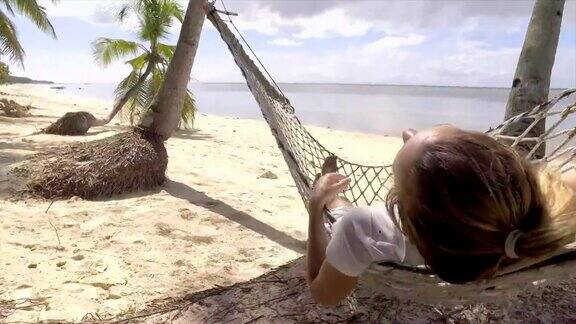 年轻女子在菲律宾热带岛屿海滩上的吊床上放松的慢动作视频高清格式人们旅游度假放松