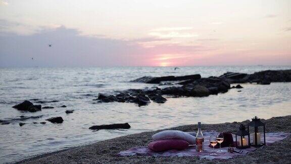 夏季海上日落浪漫的海滩野餐一瓶酒玻璃杯蜡烛格子呢和枕头