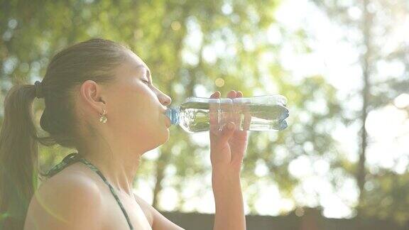 一个年轻的女人在炎热的夏天愉快地喝着瓶子里的水
