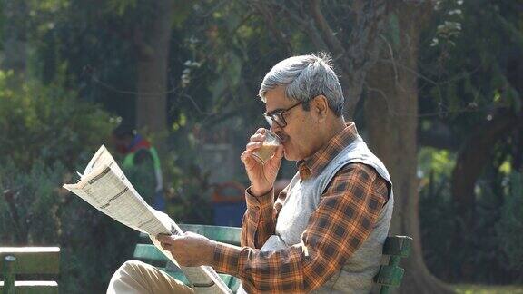 老人在公园长椅上喝茶看报纸