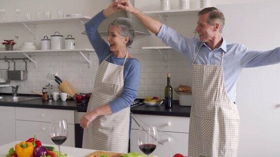 快乐的老夫妇在厨房跳舞准备健康的饭菜玩得很开心