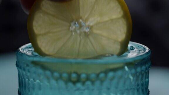 柠檬片在女士的手蘸水和冰块在蓝色玻璃杯圆形柠檬片与饮料在慢镜头宏观