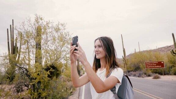 慢动作年轻快乐微笑的旅行者女人在国家公园游览期间用智能手机拍照的仙人掌沙漠