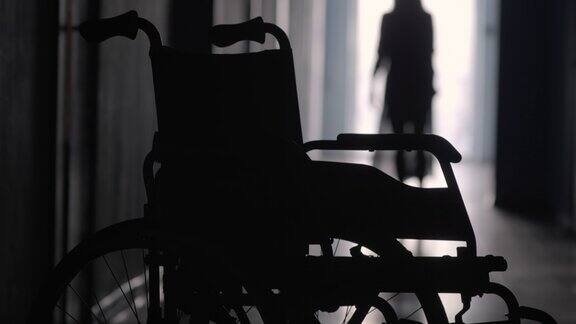 沿着医院走廊跛着走向轮椅的女人的剪影