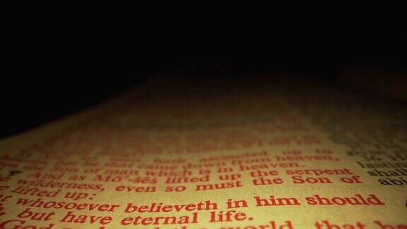 极端微距特写移动滑块拍摄的圣经突出耶稣的话约翰福音3:16在基督教圣经国王詹姆斯翻译与红色字母的话语在一个黑暗的背景与独特的照明