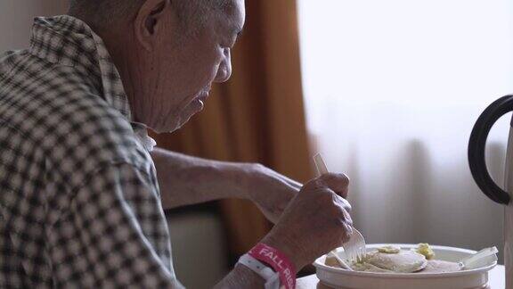 一位亚洲华人老年男病人坐在病房的床上吃早餐在煎饼上涂黄油