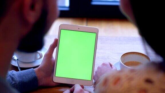 情侣们在喝咖啡休息时使用绿色屏幕的平板电脑