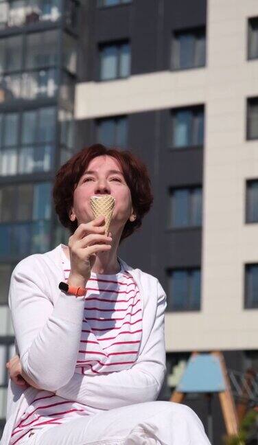 一个女人坐在城市街道的长椅上享受着冰淇淋蛋筒