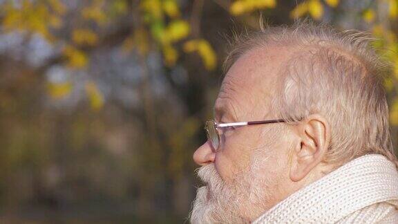 灰色头发的男人戴着眼镜走在秋天的公园里男人的脸特写