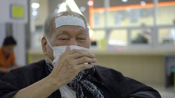 年长的亚洲人戴着口罩在医院等待时咳嗽