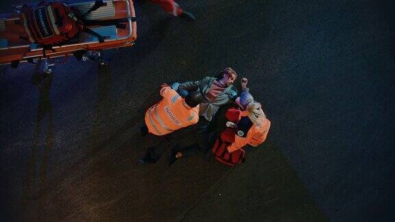 航拍的一个年轻的受伤男子卷入交通事故正在被医疗小组的紧急医疗护理人员拯救在街道上的夜晚紧急护理助理提供基本的急救帮助