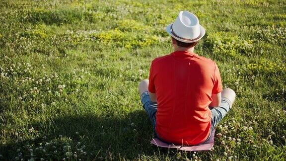 一个戴着帽子的男人坐在草地上在一个阳光明媚的日子后视图夏天的时间copyspace