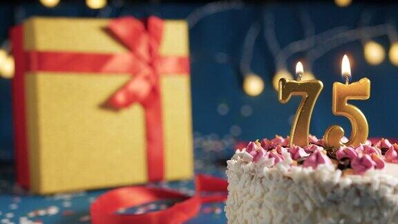 75号白色生日蛋糕金色蜡烛用打火机点燃蓝色背景用彩灯和黄色礼盒用红丝带绑起来特写镜头