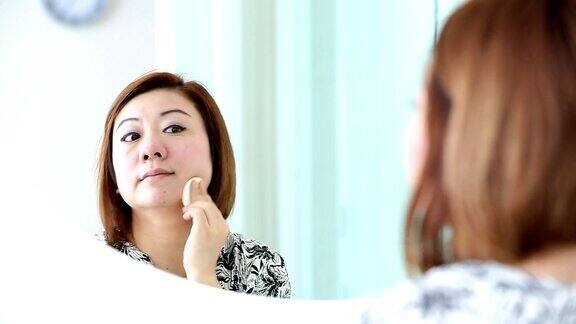 亚洲女人在卧室里化妆看着镜子