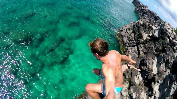 POV慢镜头年轻人从悬崖上跳到海里极限悬崖跳有趣的夏季生活方式
