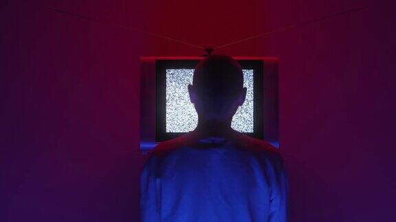 一个秃顶的男人坐在黑暗的房间里的电视机前电视机的静电噪音在画面中央