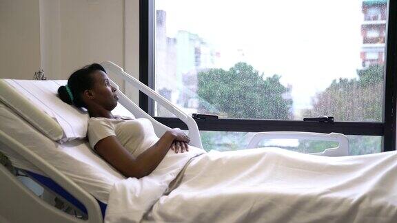 黑人女病人躺在病床上望着窗外的雨景
