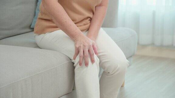 一位亚洲老太太坐在家里客厅的沙发上忍受着膝盖的疼痛