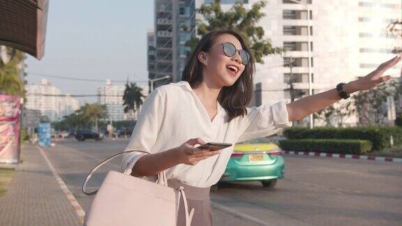 亚洲女商人穿着时尚的办公室服装在公路上打车拿着智能手机站在城市现代城市的户外