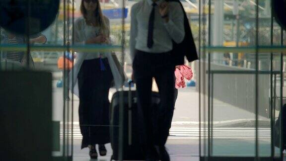 穿着长裙的男男女女通过自动打开的门进入机场大厅