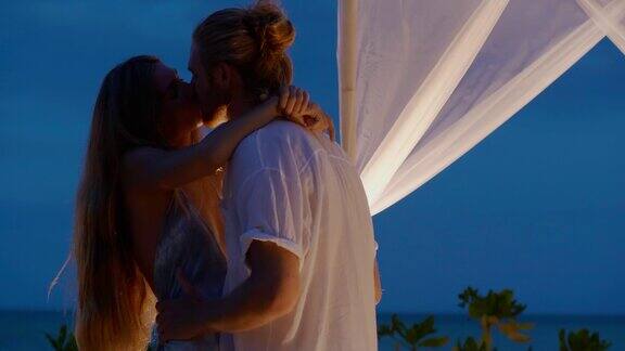 美丽的相爱的夫妇25岁一起跳舞一起亲吻在美丽的黄昏下在海边的沙滩上享受浪漫的情人节晚餐白人的蜜月